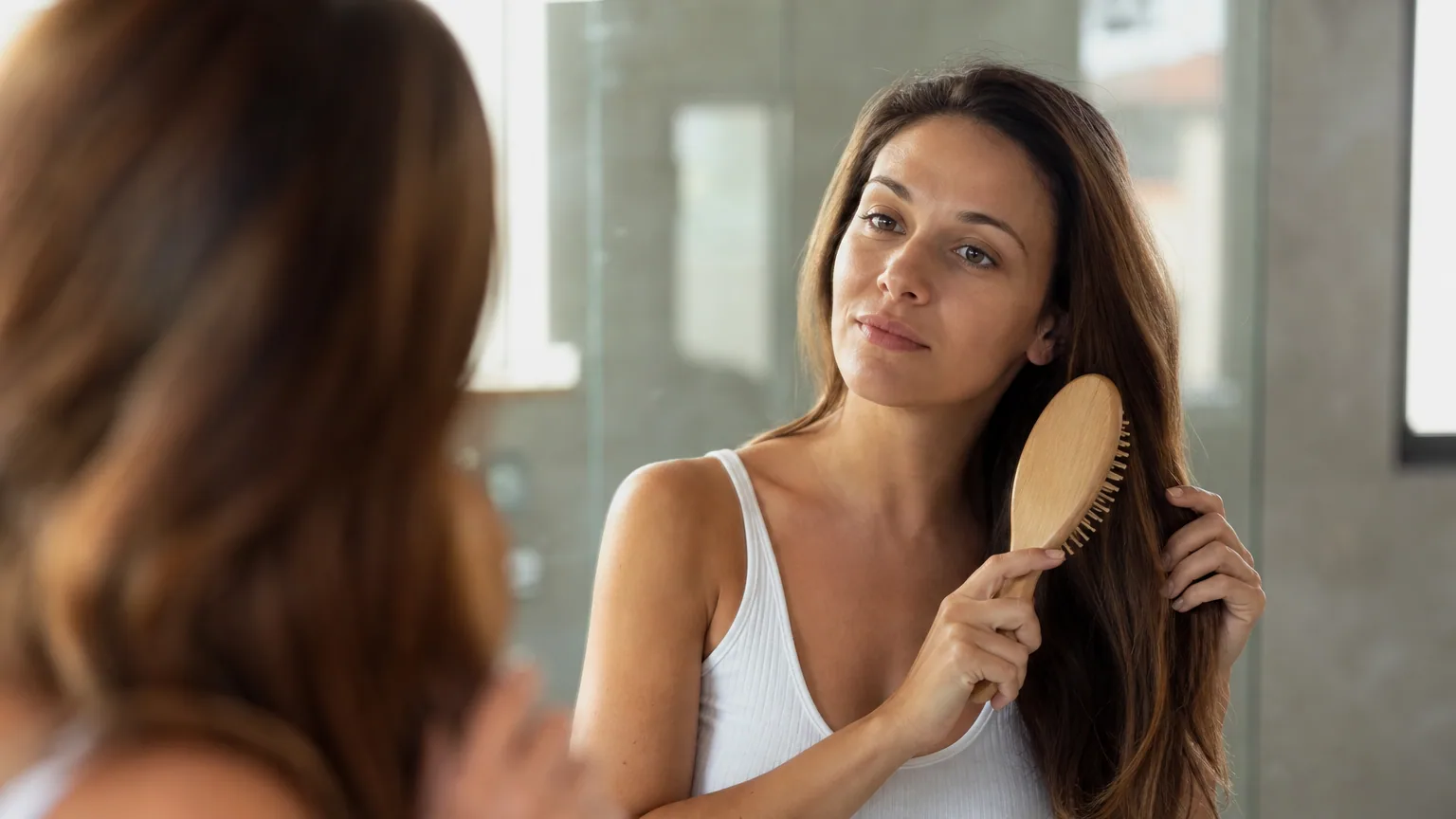 Une femme brosse ses cheveux devant un miroir dans une salle de bain lumineuse