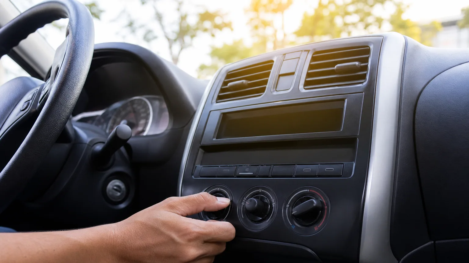 Main réglant la climatisation sur le tableau de bord d'une voiture, vue depuis l'habitacle en plein été