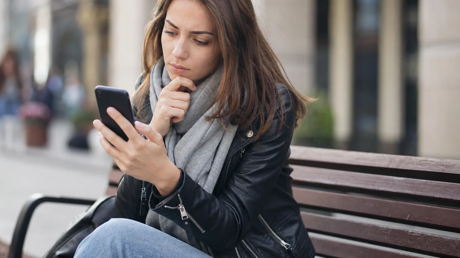 Une femme compare des offres sur son smartphone, assise sur un banc en ville