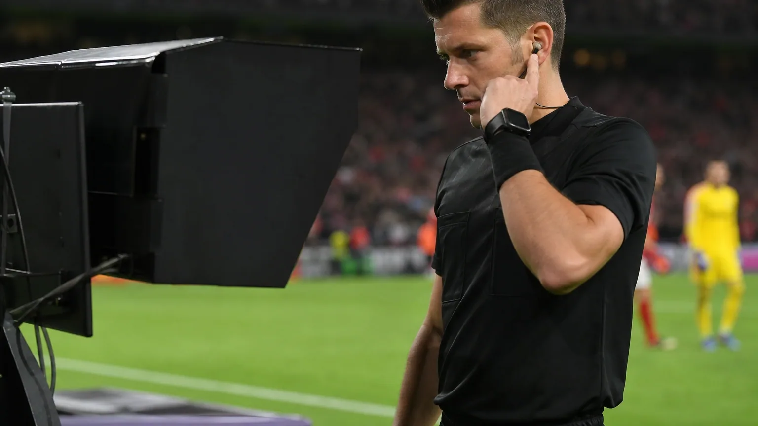 Un arbitre consulte le moniteur vidéo en bord de terrain lors d'un match de football en soirée