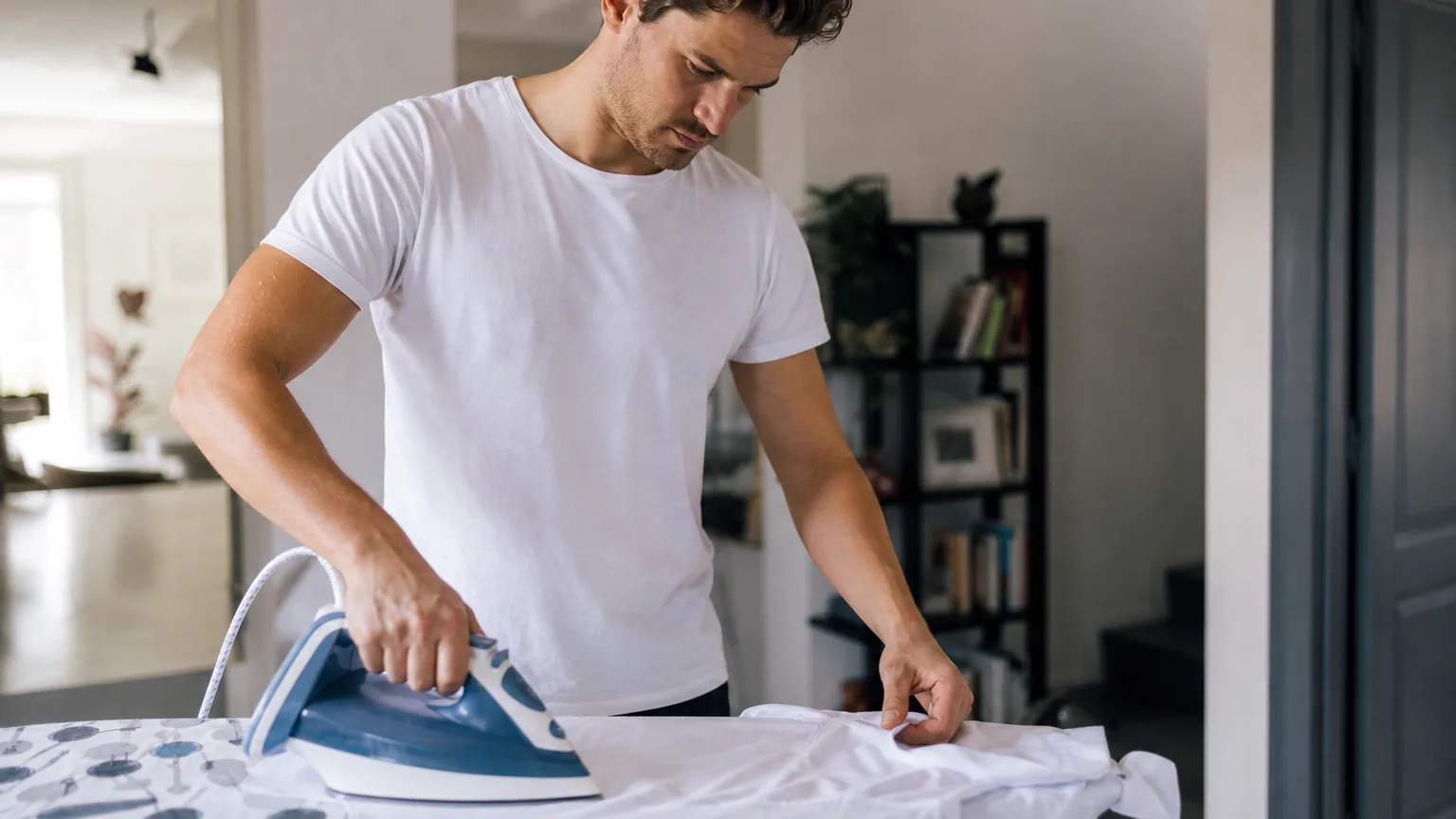 Une personne repasse une chemise blanche sur une table à repasser