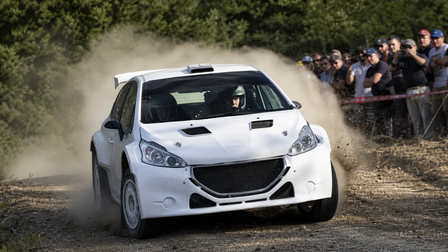 Une voiture de rallye soulevant un nuage de poussière sur une spéciale en forêt devant des spectateurs