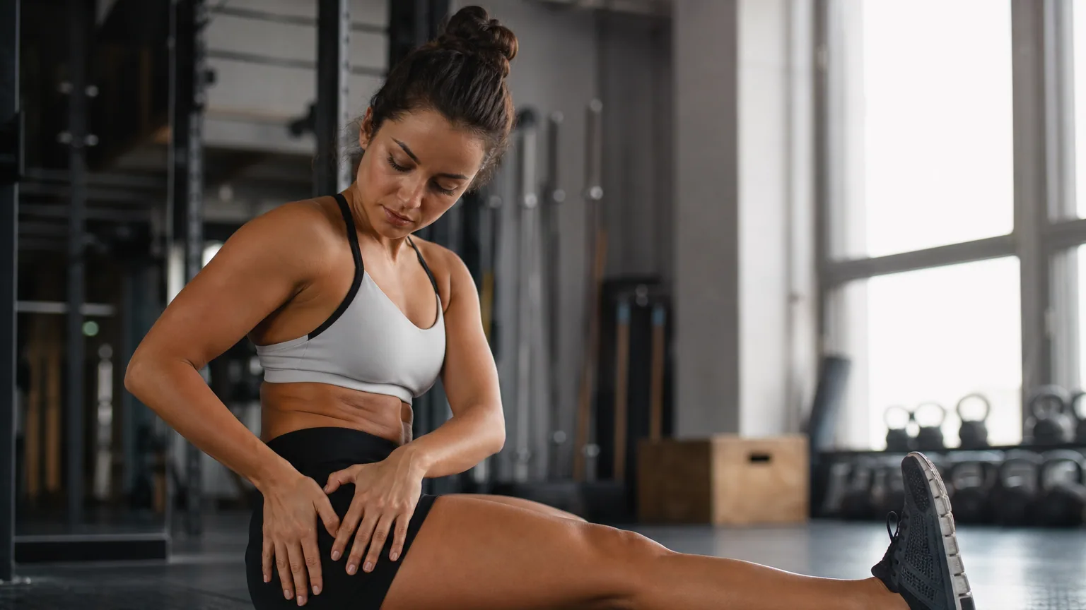 Personne assise au sol après une séance de sport, une main posée sur la cuisse, en train de s'étirer les jambes