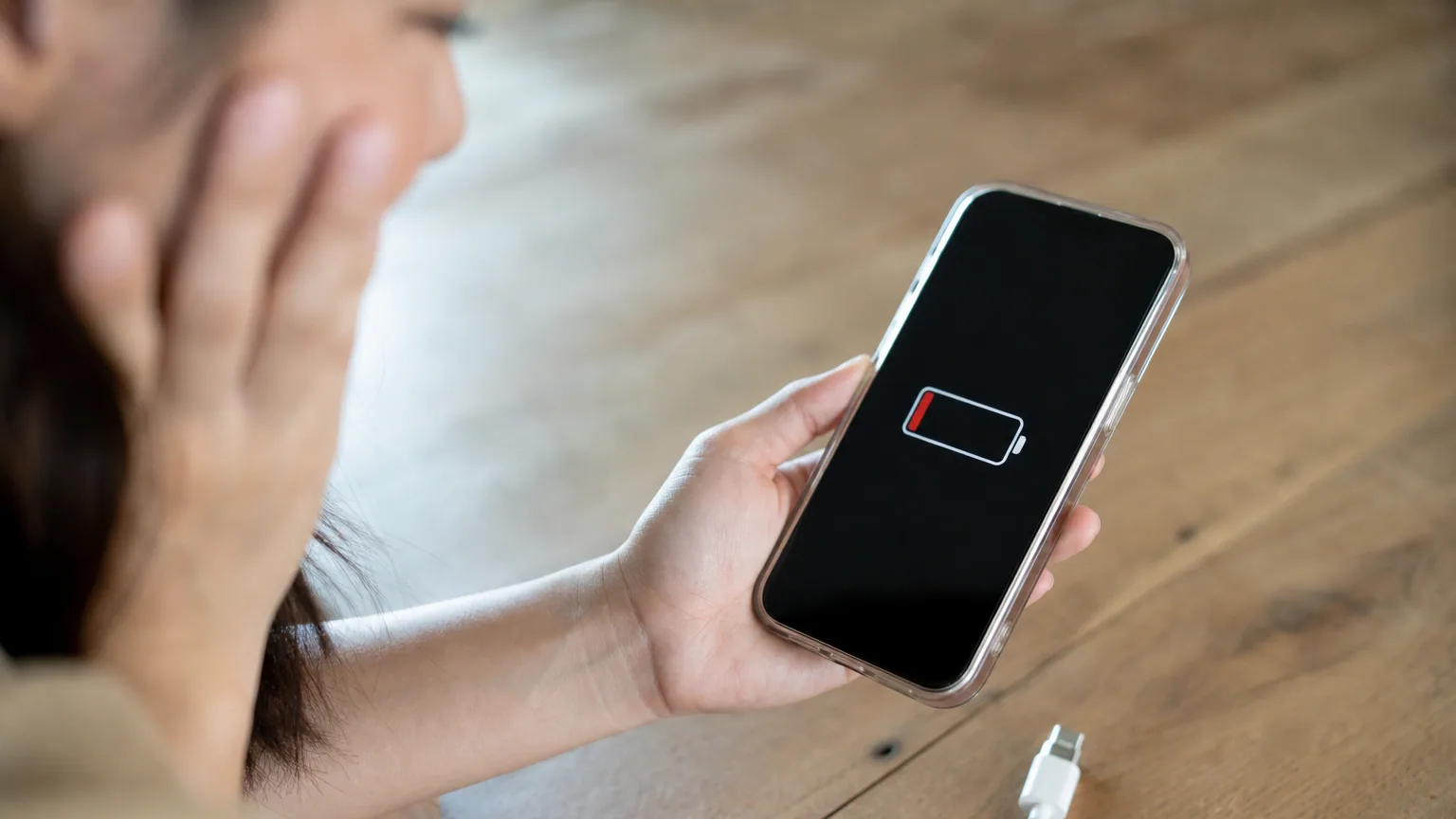 Une personne tient un smartphone affichant une batterie faible près d'un câble de recharge