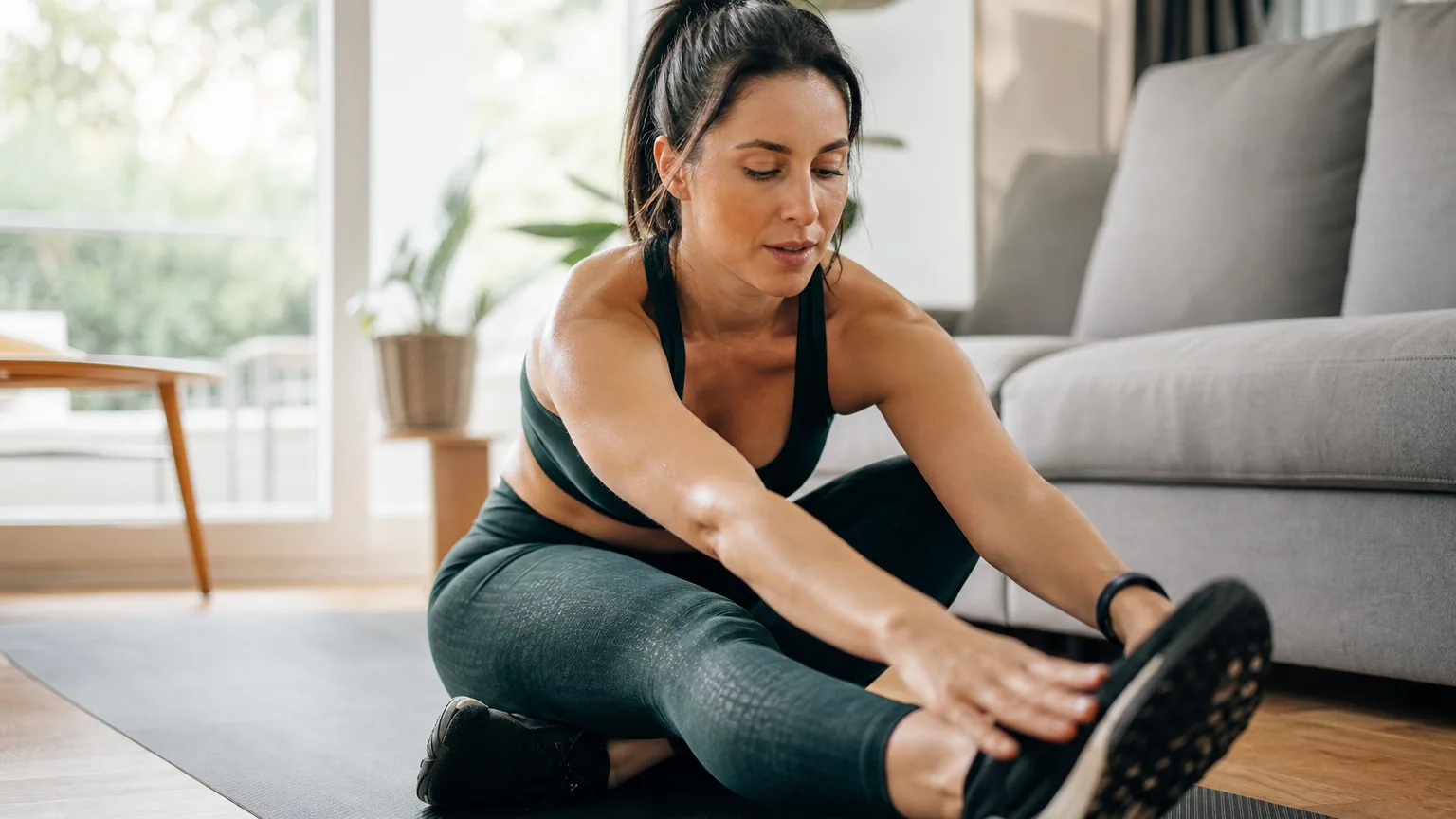 Une sportive réalise des étirements assise sur un tapis après sa séance
