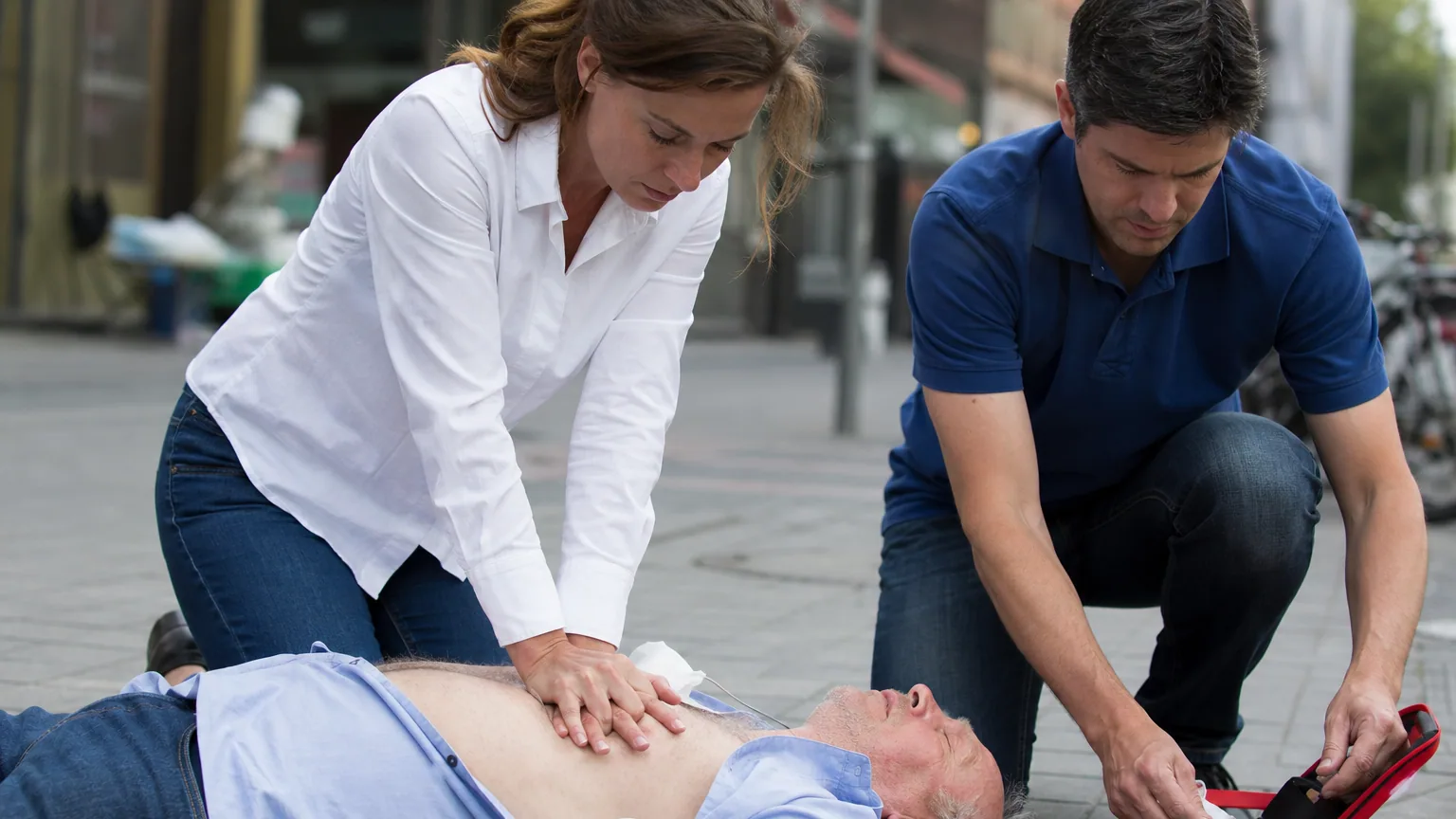 Deux passants pratiquent un massage cardiaque et préparent un défibrillateur sur une victime au sol