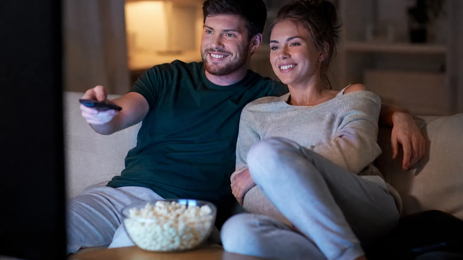 Un couple regarde une série à la télévision le soir dans un salon éclairé par l'écran