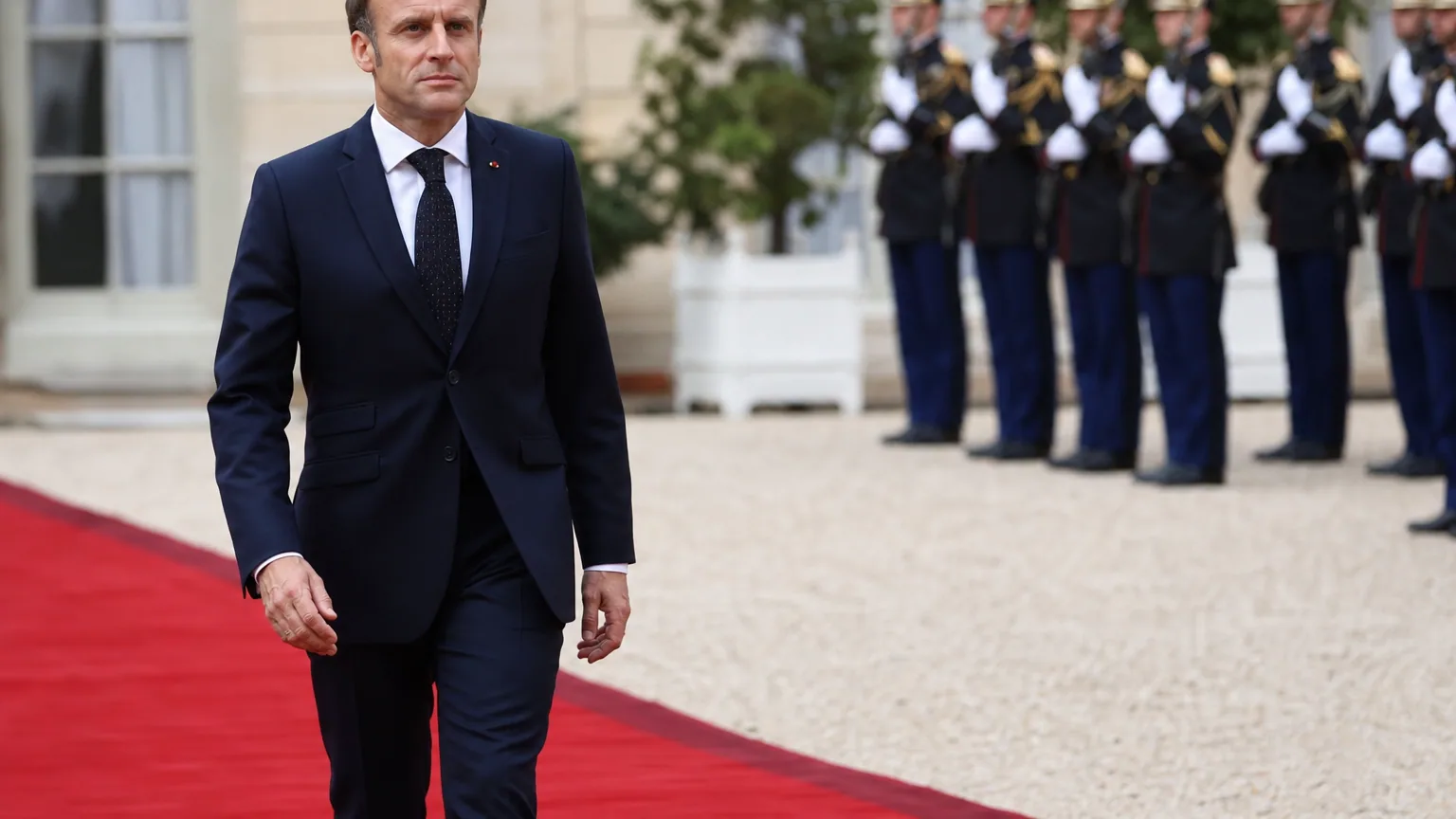 Un chef d'État français traverse la cour d'un palais présidentiel devant la garde républicaine au garde-à-vous.