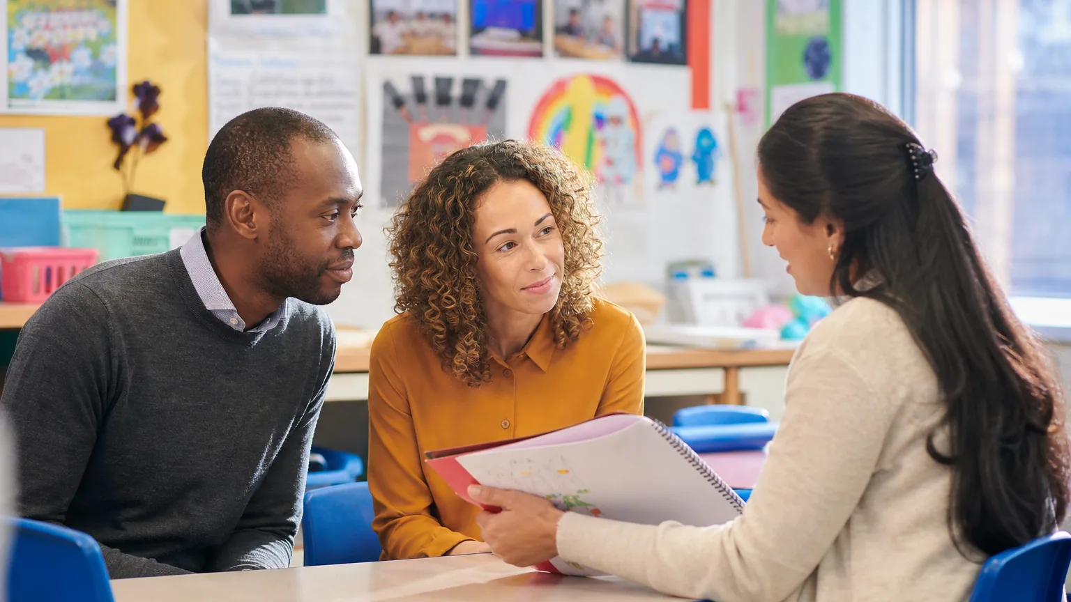 Parents échangeant avec une enseignante autour d'une table dans une salle de classe