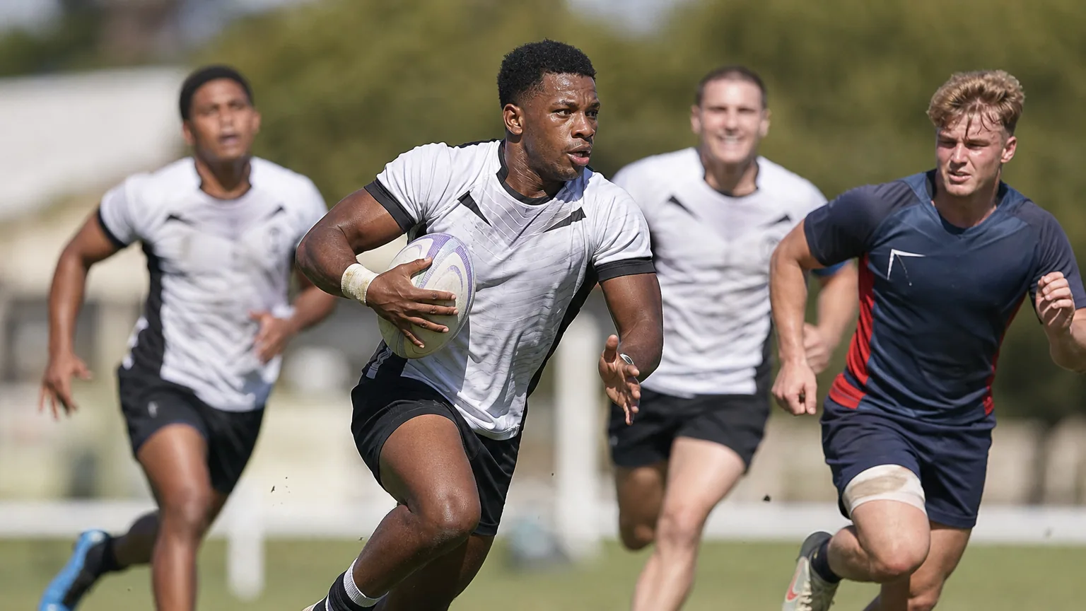 Des joueurs de rugby à 7 courent avec le ballon sur un terrain ensoleillé