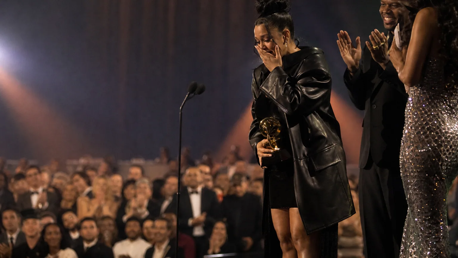 Un artiste ému tient un trophée sur la scène illuminée d'une cérémonie de récompenses musicales